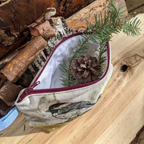 plant dyed zippered pouch that is block printed with a chickadee, with the zipper open showing some pinecones inside