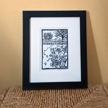 Framed print of a garden in winter, with dried flowers and animal tracks in the foreground, and a fence and some bare trees in the background